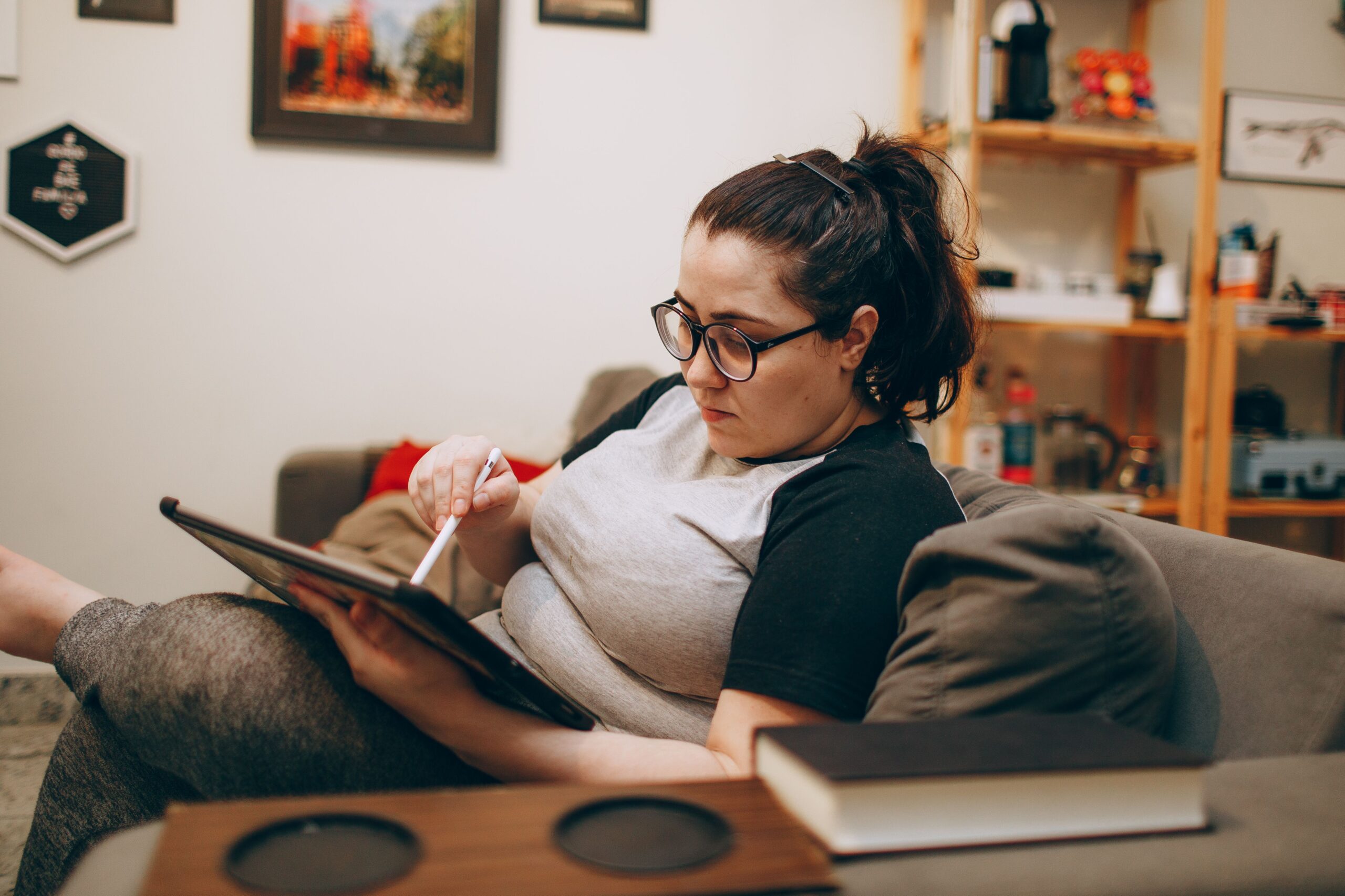 Woman wearing glasses, relaxing on couch while using tablet.